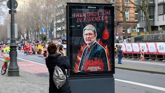Eine Frau macht ein Foto von dem Plakat gegen Kardinal Woelki und das Kölner Erzbistum.
