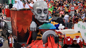 Ein Mottowagen des Kölner Rosenmontagszugs zeigt Putin als blutdürstigen Vampir, der die Ukraine durch einen Fleischwolf dreht. Verkleidete säumen den Zugweg.