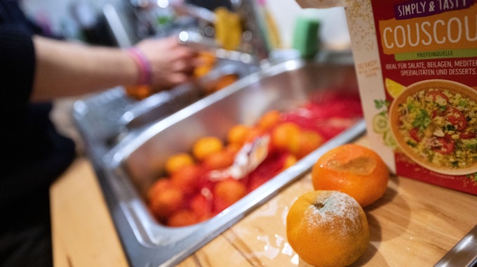 Einzelne schimmelige Mandarinen liegen aussortiert auf einer Küchenarbeitsplatte, während eine Frau andere unverdorbene Mandarinen wäscht.