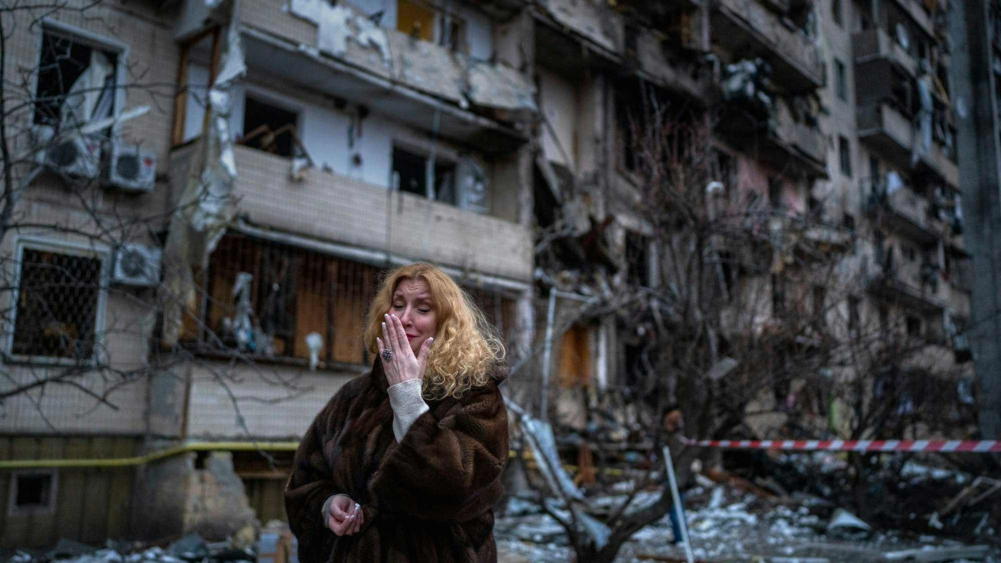 Eine Frau steht weinend vor den Trümmern eines Hochhauses in Mariupol. Im Hintergrund sind zerstörte Wohnhäuser zu erkennen.