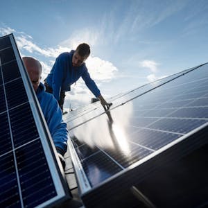 Zwei Männer montieren Photovoltaikmodule auf dem Dach eines Wohnhauses.