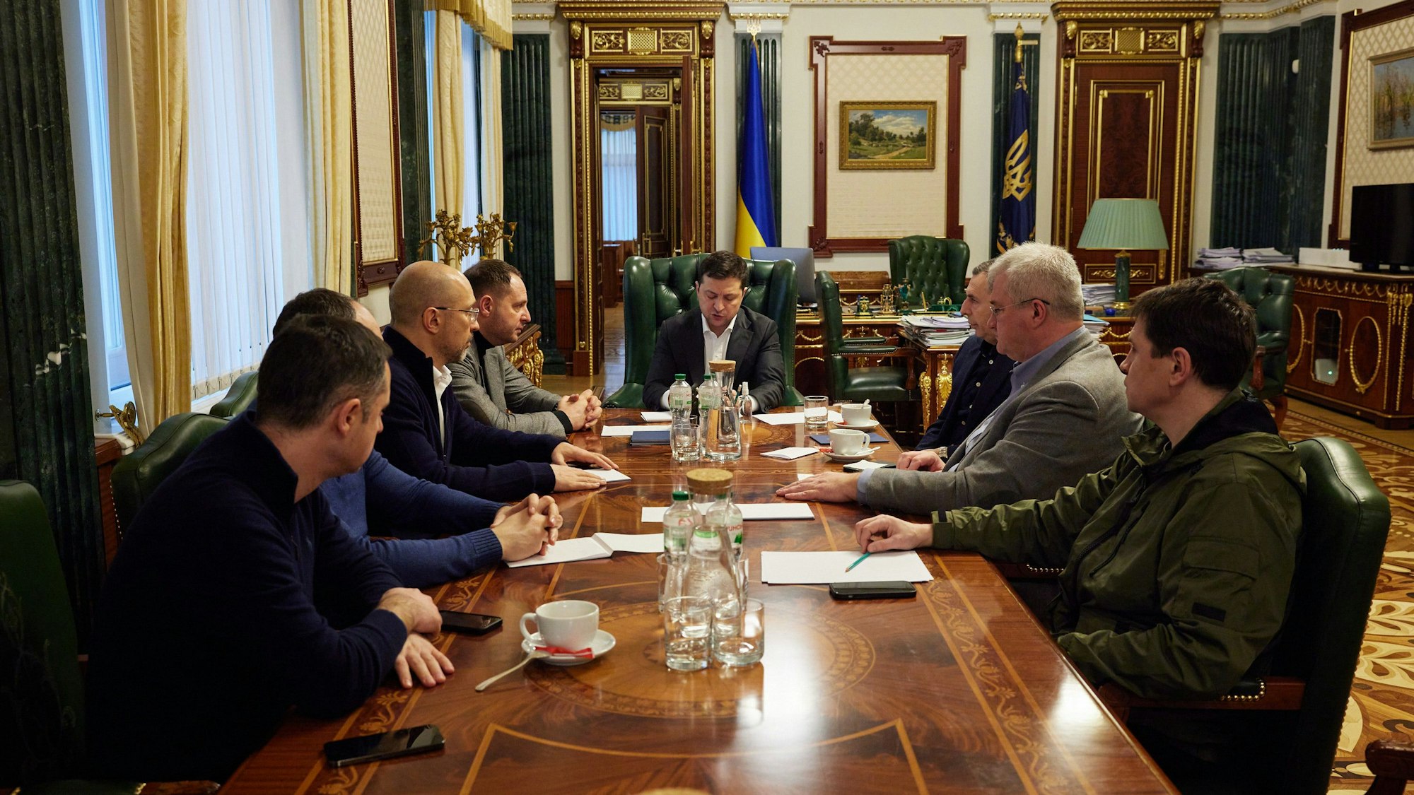 Der ukrainische Präsident Wolodymyr Selenskyj sitzt in der Mitte eines Tisches. Links und rechts von ihm sitzen sieben weitere Männer.