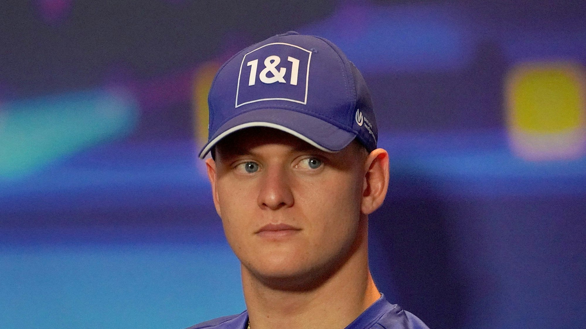 Mick Schumacher blickt auf einer Pressekonferenz in Abu Dhabi vom Podium in Richtung Presse. Er trägt eine blaue Kappe seines Teams Haas.