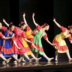 Sechs junge Mädchen in roten, blauen, gelben und grünen Kleidern zeigen einen Balletttanz.
