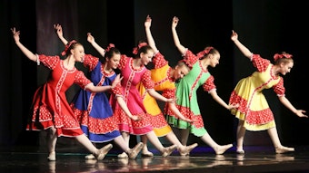 Sechs junge Mädchen in roten, blauen, gelben und grünen Kleidern zeigen einen Balletttanz.