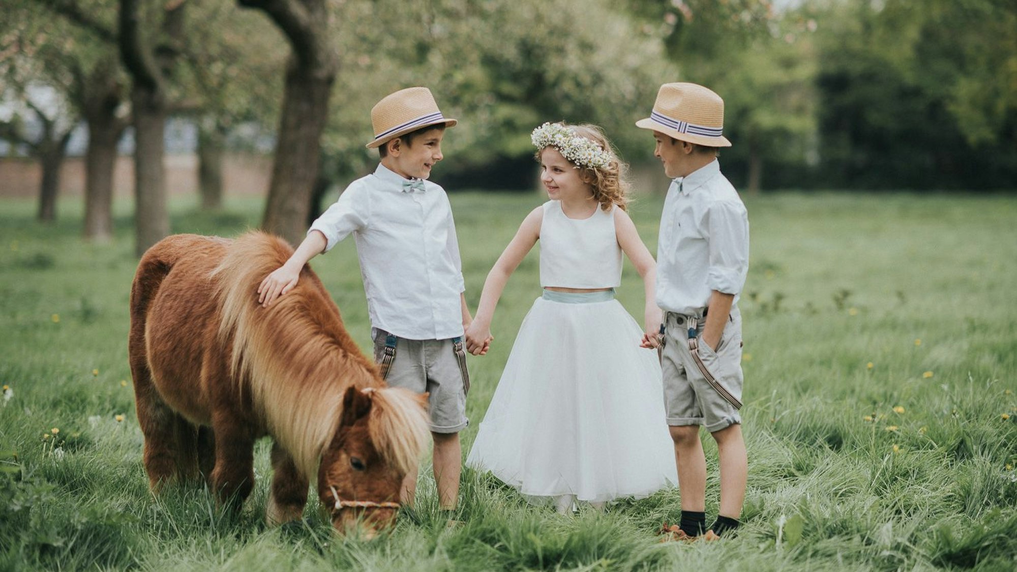 Es sind drei Kinder zu sehen, die mit einem Pony auf einer Wiese stehen.