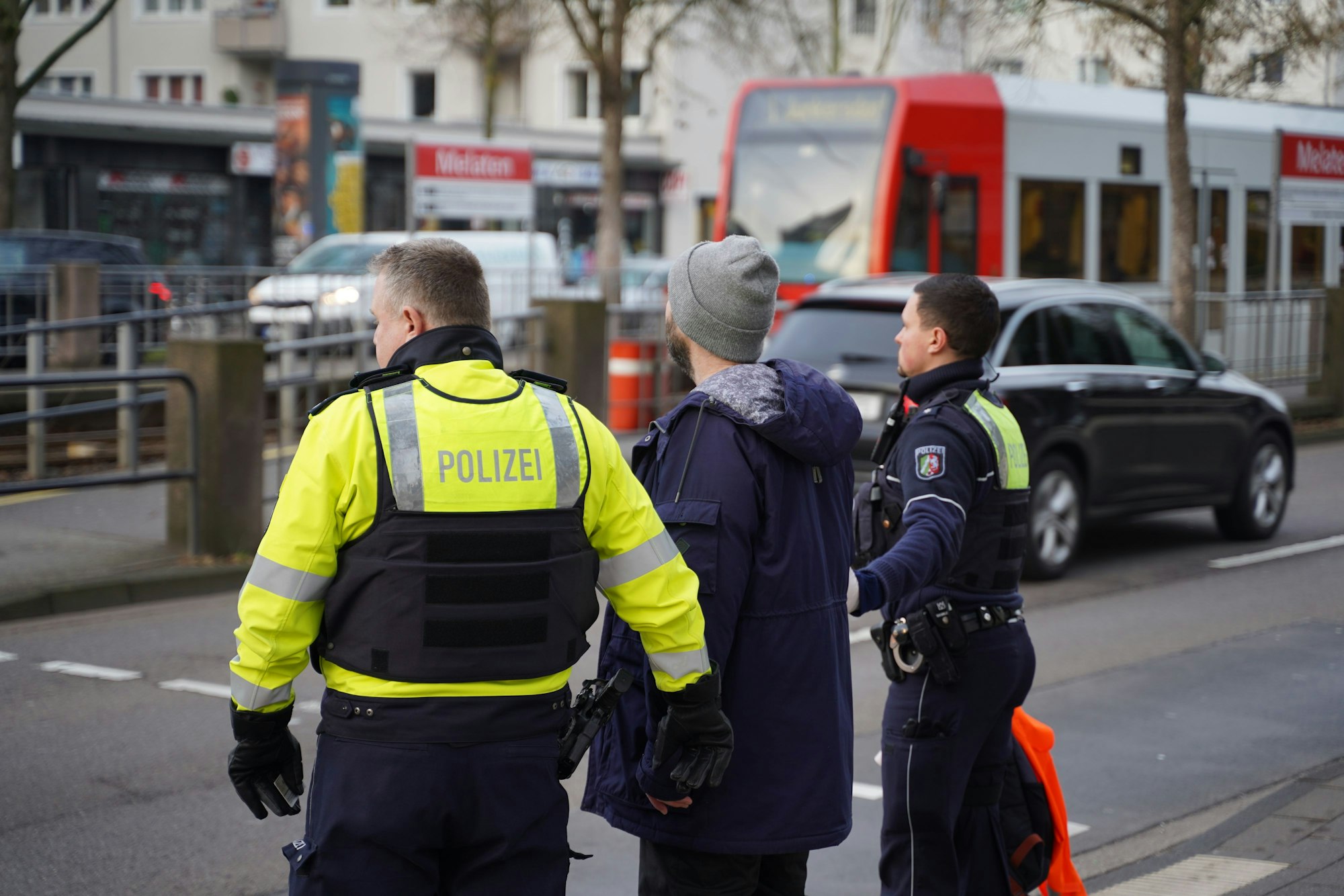 Ein Aktivist von „Letzte Generation“ wird von der Polizei abgeführt. Er wollte sich auf der Aachener Straße in Höhe der U-Bahnhaltestelle Melaten festkleben.