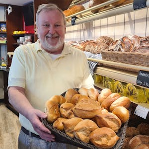 Das Foto zeigt Bäcker Willi Immerath. Er hält einen Korb frischer Brötchen in beiden Händen.