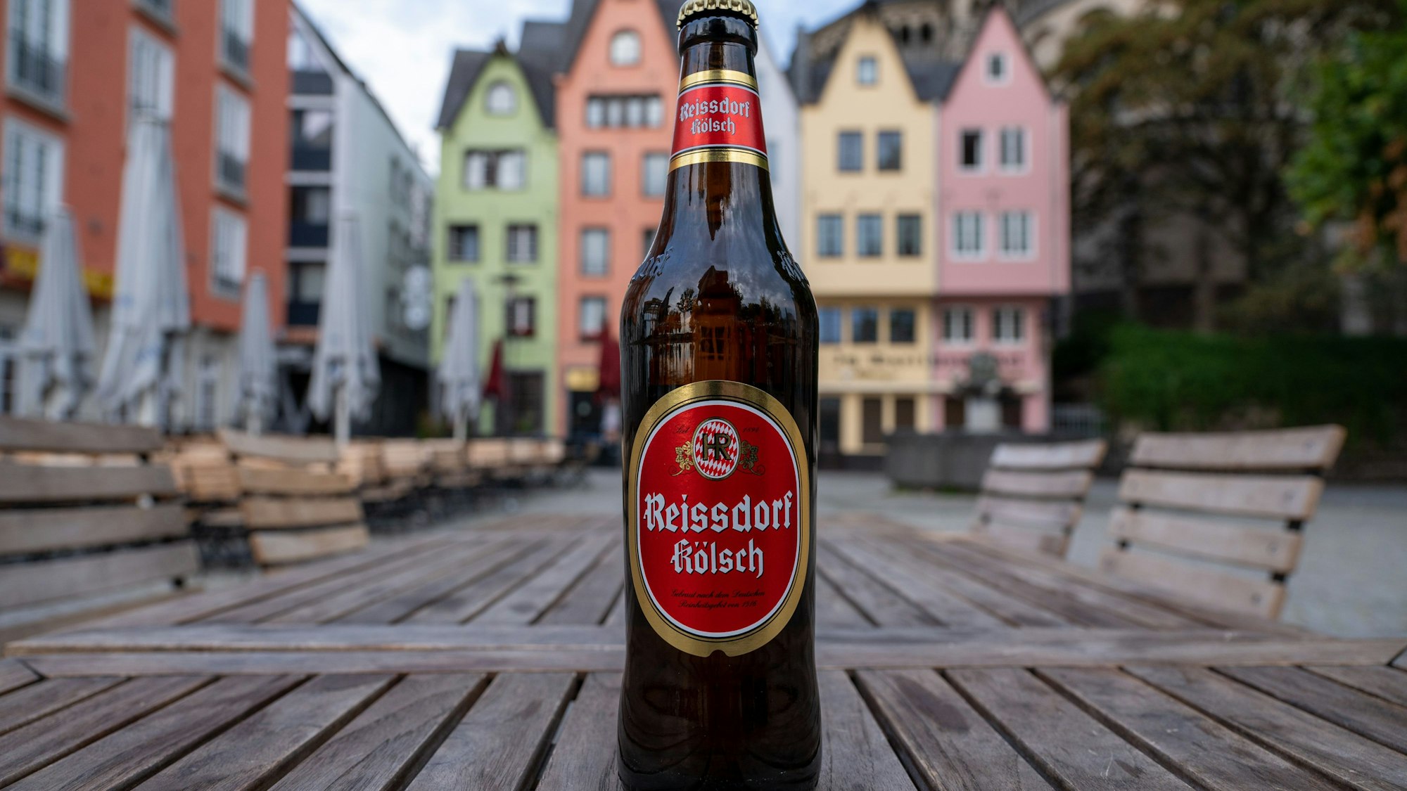 Reissdorf Kölsch-Flasche steht auf einem Tisch vor bunten Häusern in Köln.