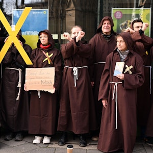 Das Foto vom 22. Februar 2023 zeigt als Mönche verkleidete Menschen vor der Grünen-Parteizentrale in Düsseldorf. Eine Person hält ein gelbes X in die Höhe.