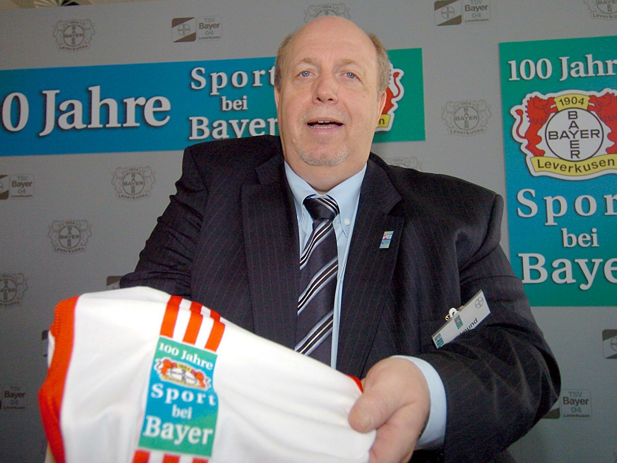 Reiner Calmund hält das Trikot zum Jubiläum von Bayer Leverkusen in der Hand.