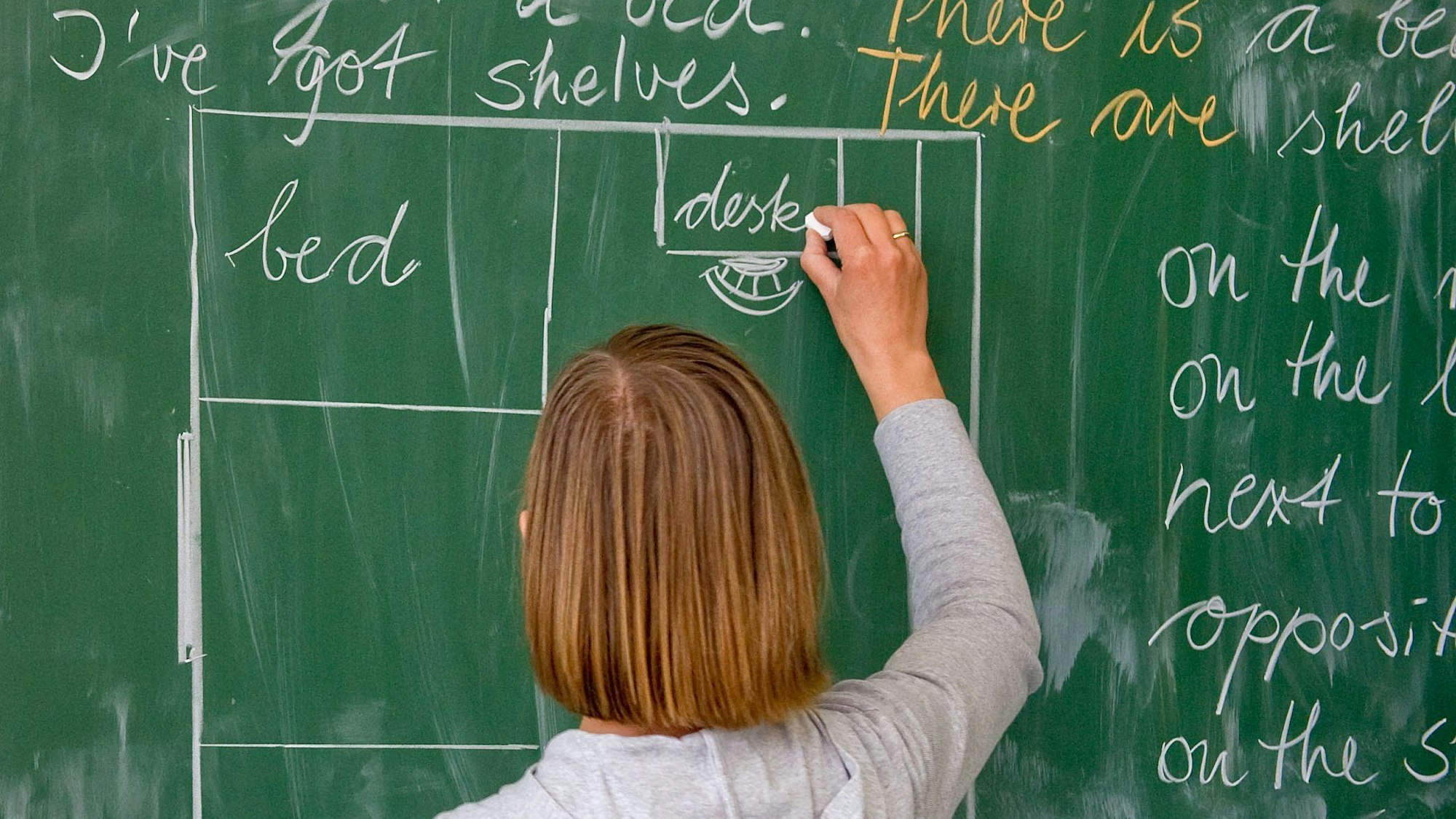 Eine Lehrerin schreibt in englischer Sprache an eine Tafel.