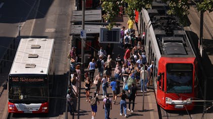 Menschen stehen an einer Bahnhaltestelle am Neumarkt, daneben eine KVB-Bahn und ein Bus.&nbsp;