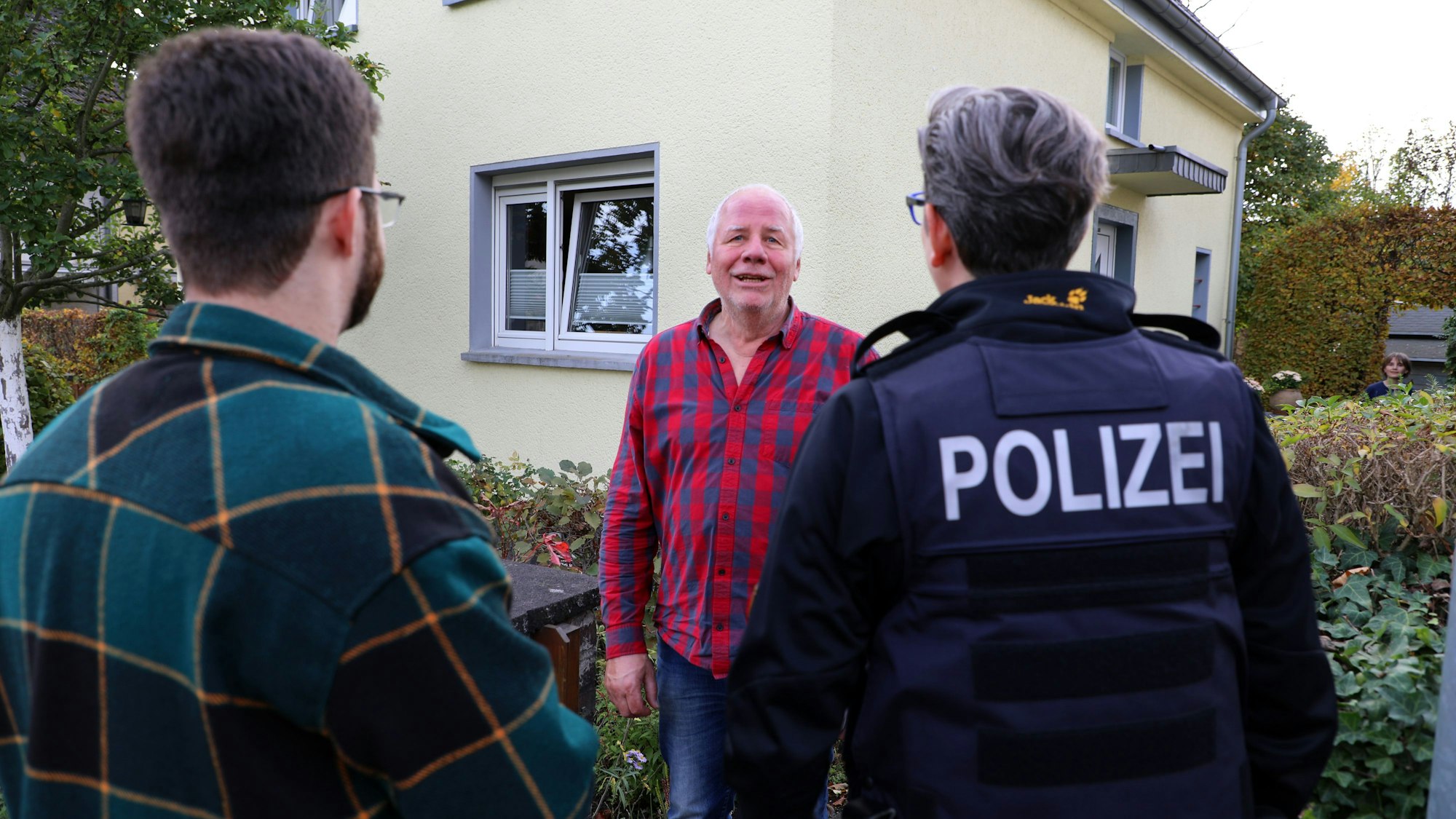 Zwei Polizeibeamte beraten einen Hausbewohner, der am Tor zu seinem Grundstück steht.