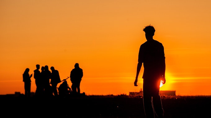 Eine Gruppe Jugendlicher als Schattenrisse im Sonnenuntergang.
