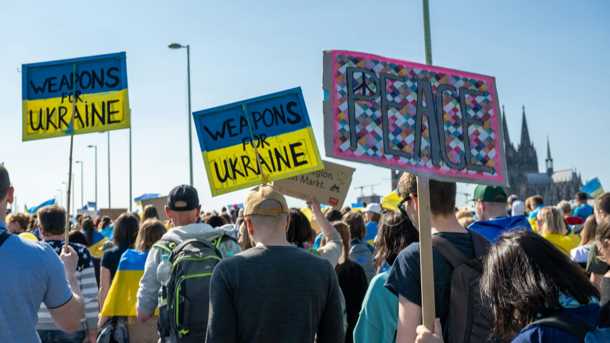 Auf Plakaten fordern Demonstranten Waffen und Frieden.