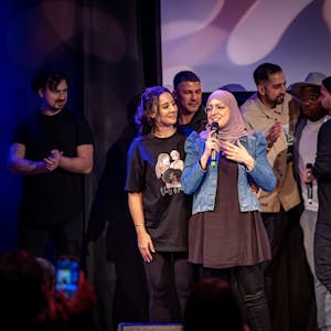 Die Veranstalterinnen stehen auf der Bühne, Asmaa El Idrissi hält ein Mikrofon in der Hand. Hinter ihnen stehen weitere Künstler, die während des Events auftraten.