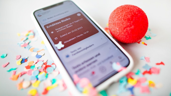 Ein Smartphone mit roter Kachel in der Corona-Warn-App liegt in Konfetti