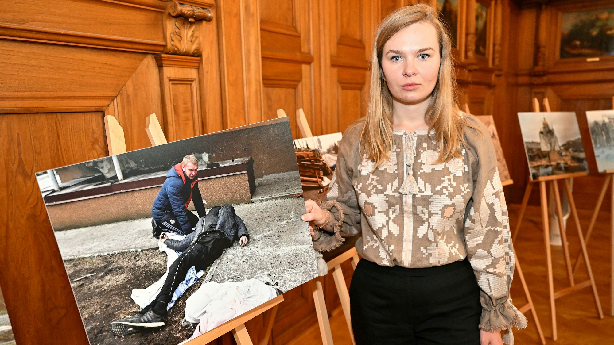 Alina Saraniuk hält ein großes Foto in der Hand. Auf dem Foto ist ein Mann zu sehen, der seinen auf der Straße erschossenen Vater findet.