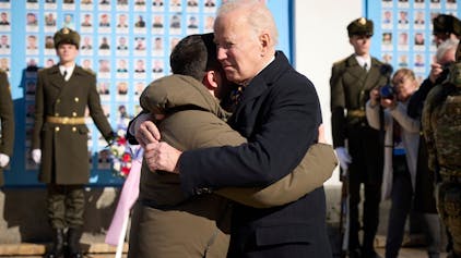 Joe Biden (Mitte r), Präsident der USA, und Wolodymyr Selenskyj, Präsident der Ukraine, umarmen sich zum Abschied an der Gedenkmauer für die gefallenen Verteidiger der Ukraine in Kiew am 20. Februar 2023. Im Hintergrund sind eine Ehrenwache ukrainischer Soldaten und ein Blumenkranz zu sehen.