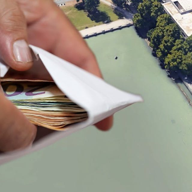 Der Aachener Weiher mit der kleinen Brücke im Hintergrund, im Vordergrund Hände, die einen Umschlag mit Geld halten