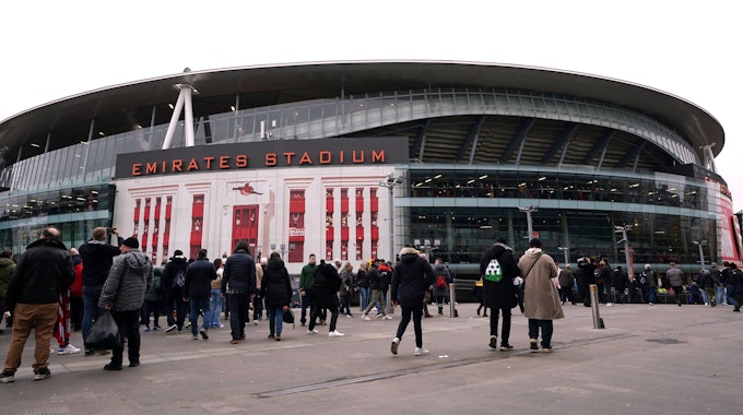 Das Emirates Stadium ist seit 2006 die Heimstätte des Premier-League-Vereins FC Arsenal. Das Foto zeigt das Stadion von außen am 11. Februar 2023, dem Tag des Arsenal-Heimspiels gegen Brentford. Fans überqueren den Vorplatz des Stadiums in Winterkleidung.