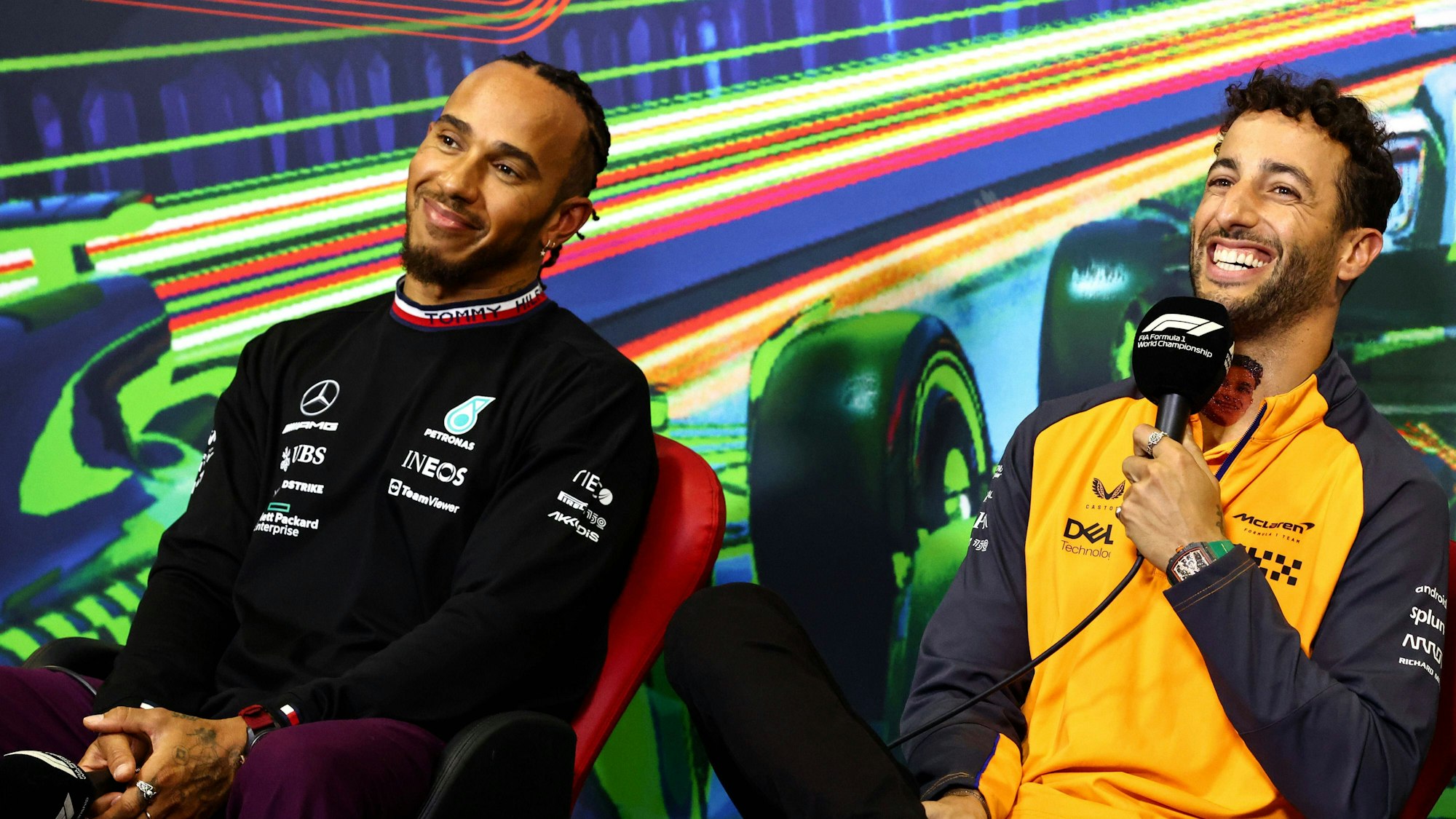 Daniel Ricciardo (r.) sitzt bei einer Pressekonferenz in einem orangen McLaren-Oberteil neben Lewis Hamilton, Formel-1-Fahrer bei Mercedes. Beide Fahrer lachen. Das Foto wurde im Rahmen des Großen Preis von Italien in Monza am 8. September 2022 aufgenommen.