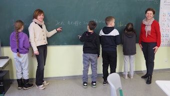Zwei Lehrerinnen stehen an einer Tafel mit vier Kindern.