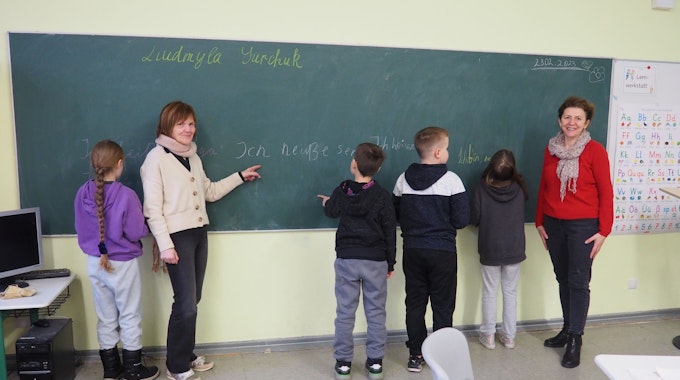 Zwei Lehrerinnen stehen an einer Tafel mit vier Kindern.