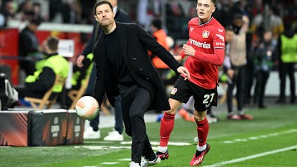 Leverkusens Trainer Xabier Alonso wirft neben Florian Wirtz einen Ball.