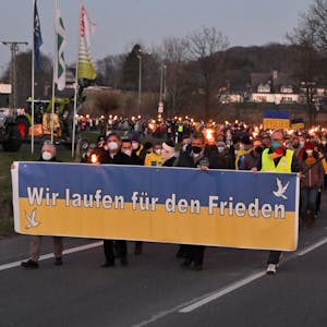 Menschen ziehen mit Fackeln und Transparenten in Kürten-Bechen eine Straße hinunter, vorne ein Banner mit der Aufschrift „Wir demonstrieren für den Frieden“.