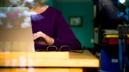 Eine Frau sitzt zuhause an einem Schreibtisch und arbeitet an einem Laptop.&nbsp;