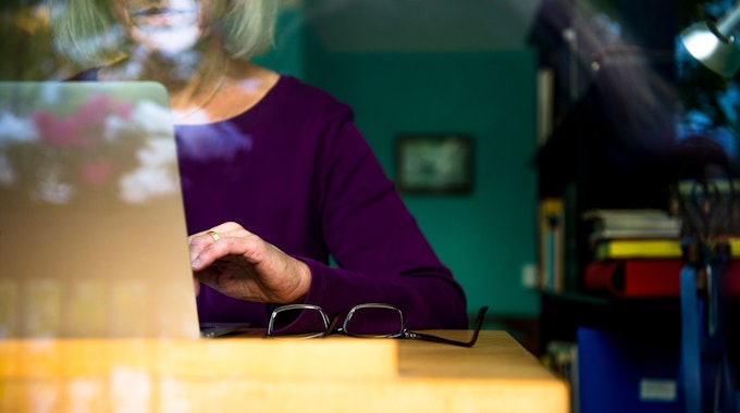 Eine Frau sitzt zuhause an einem Schreibtisch und arbeitet an einem Laptop.