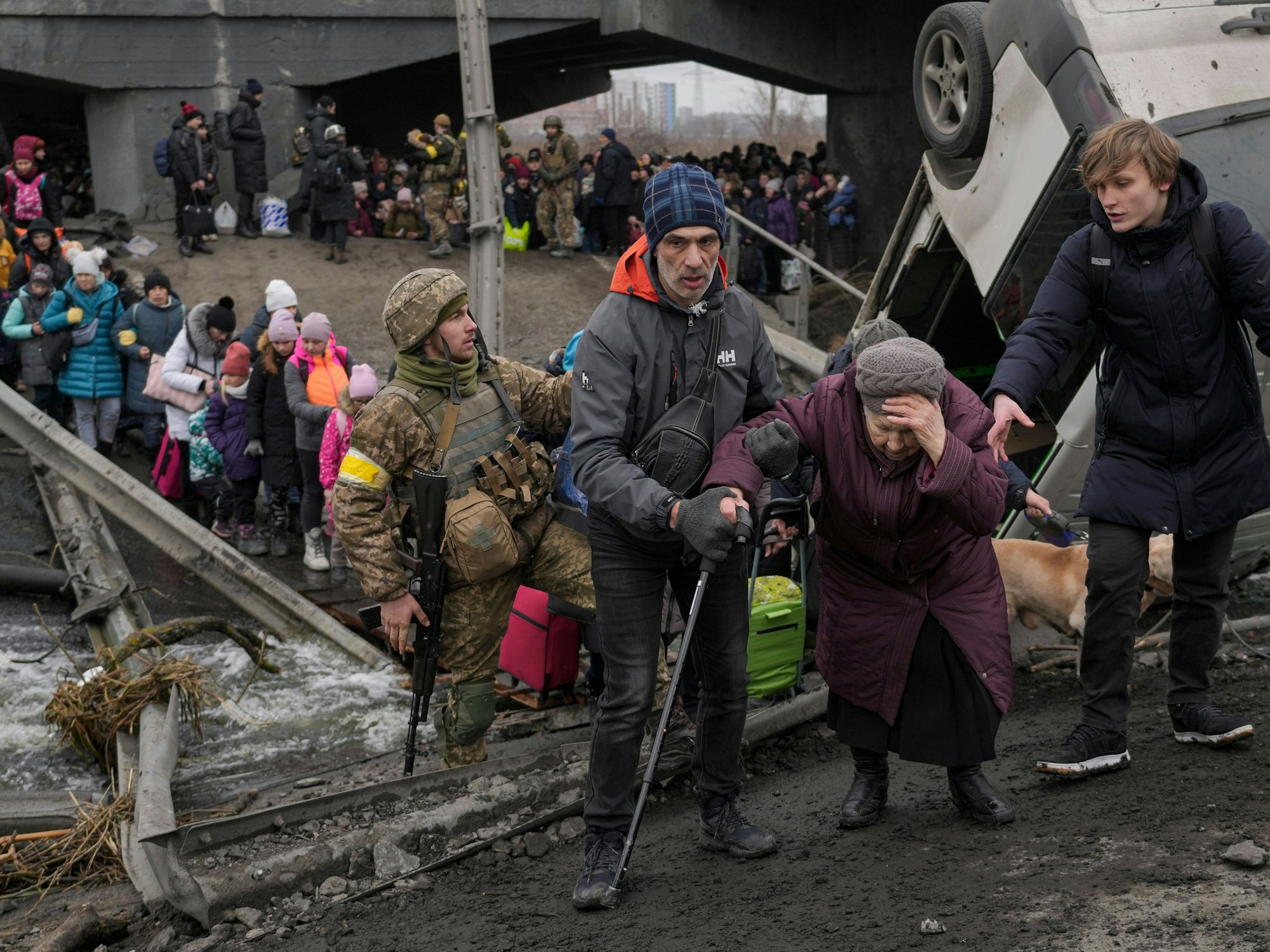Eine ältere Dame wird bei der Überquerung des Flusses Irpin unter einer zerstörten Brücke unterstützt, während Zivilisten aus der Stadt fliehen.