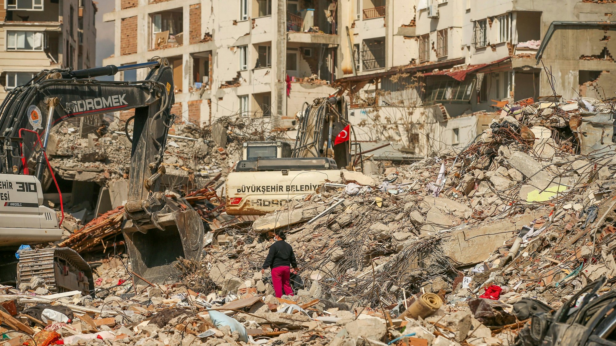 Ein Mann steht zwischen Trümmern, während Bagger die Überreste eines zerstörten Gebäudes nach dem Erdbeben abreißen.