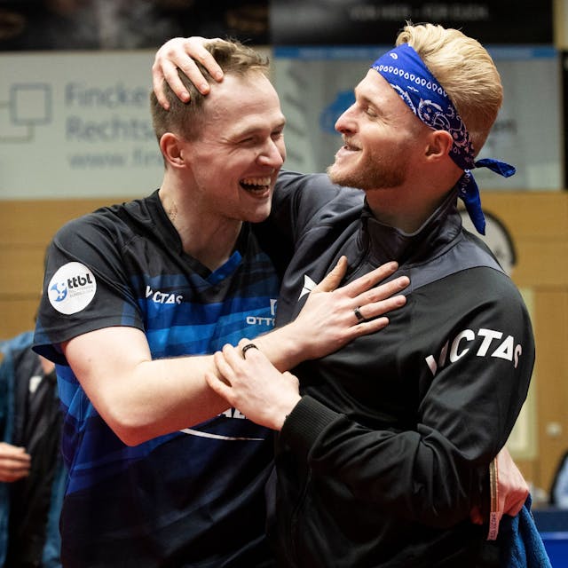 Zwei Tischtennisspieler liegen sich lachend in den Armen.