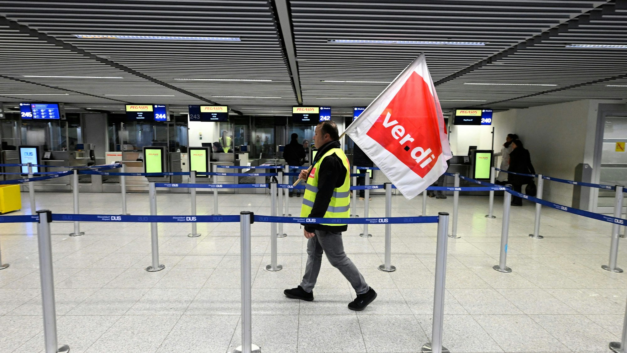 Mann mit Verdi-Fahne geht durch den Flughafen in Düsseldorf.