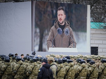 Das Foto zeigt den ukrainischen Präsidenten Wolodymyr Selenskyj. Er spricht vor uniformierten Soldaten, seine Rede wird auf eine große Leinwand übertragen.