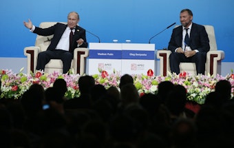 Der russische Oligarchen Oleg Deripaska (r.) sitzt gemeinsam mit dem russischen Präsidenten Wladimir Putin (l.) auf einer Bühne.