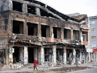 Das Foto zeigt eine Frau, die an einem zerstörten und ausgebrannten Gebäude im ukrainischen Charkiw vorbeigeht.