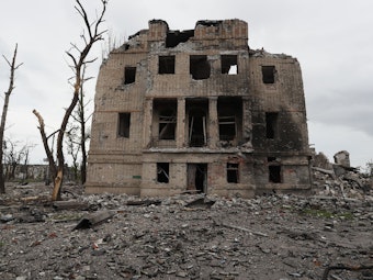 Das Foto zeigt das zerstörte Stahlwerk Asowstal in der ukrainischen Stadt Mariupol. Das Gebäude hat Brandspuren, alle Fenster und Türen fehlen, der obere Bereich ist eingebrochen. Die Umgebung ist ein Trümmerfeld, überall liegen Teile des ehemaligen Stahlwerks.
