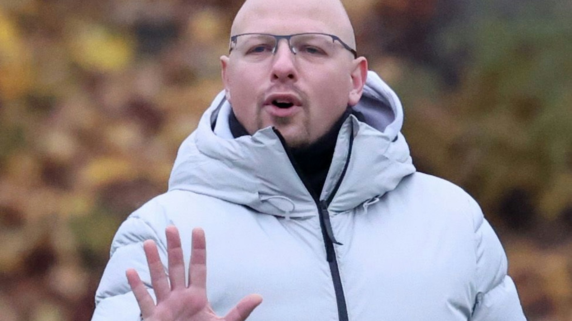 Trainer Stefan Müller trägt eine helle Winterjacke und hebt eine Hand.