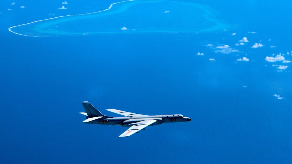 Auf dem Bild ist ein chinesisches Kampfflugzeug zu sehen. Es schwebt über einer Inselgruppe im Südchinesischen Meer.+