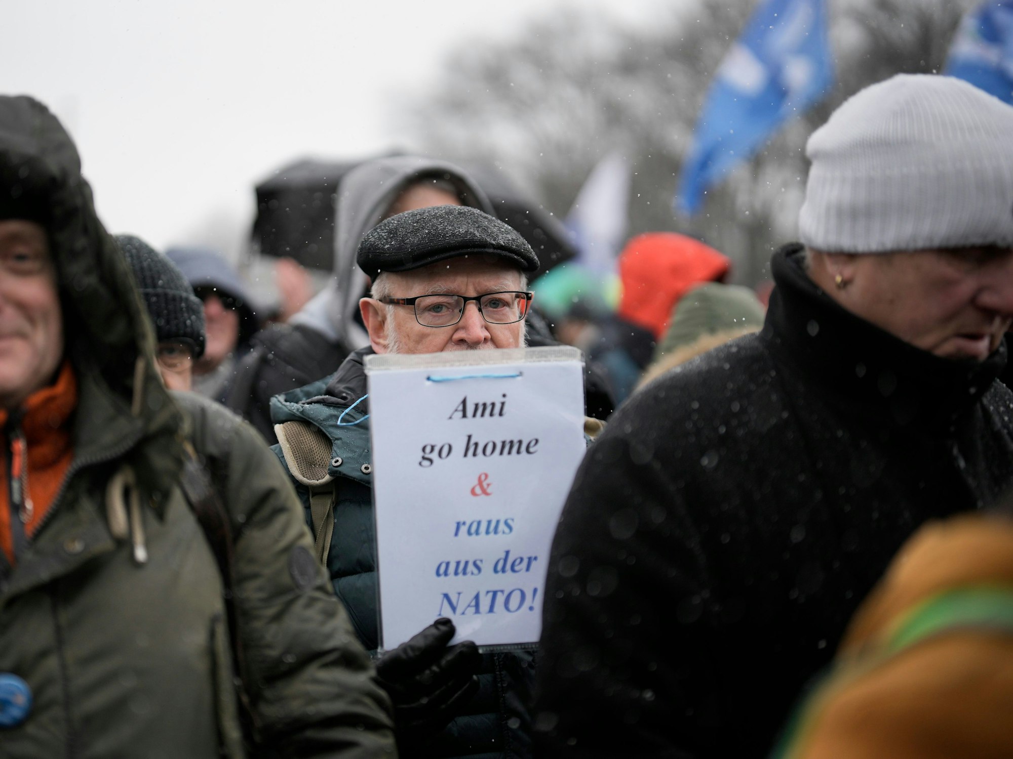 Ein Mann hat ein Schild mit der Aufschrift „Ami go home & raus aus der NATO"“ in der Hand.