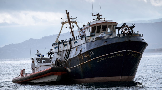 Patrouillenboot fährt mit dem Boot der Migranten in den Hafen ein.&nbsp;
