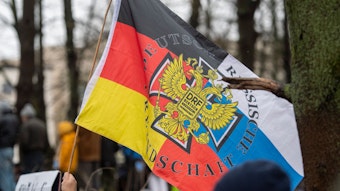 Ein Teilnehmer einer Demonstration für Verhandlungen mit Russland am Brandenburger Tor trägt eine Flagge mit Deutschen und Russischen Farben.