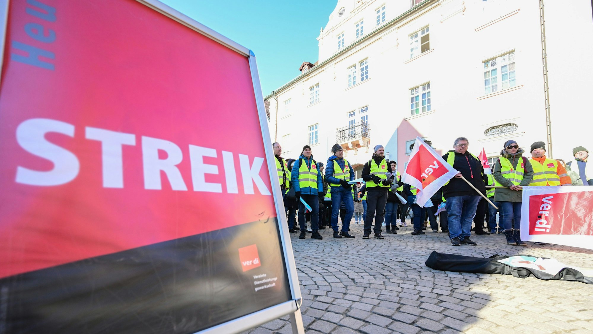 Mitglieder der Gewerkschaft Verdi stehen bei einer Kundgebung mit Fahnen auf einem Marktplatz in Rottenburg, Baden-Württemberg.