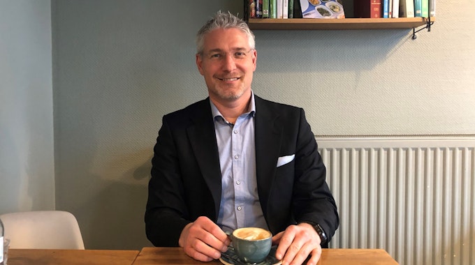 Martin Sagel aus Kerpen sitzt im Anzug in einem Café. In seinen Händen hält er einen Cappuccino.
