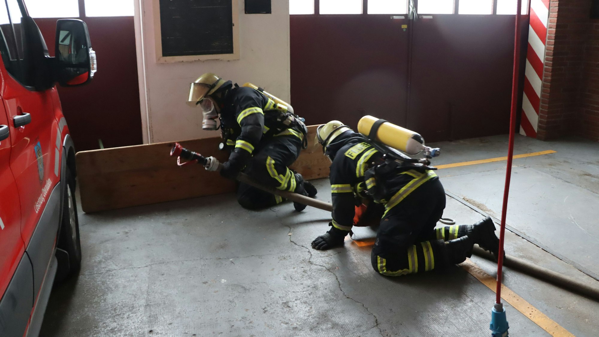 Das Foto zeigt zwei angehende Feuerwehrleute bei der Suche nach Vermissten. Sie bewegen sich auf Knien rutschend durch den Raum fort.
