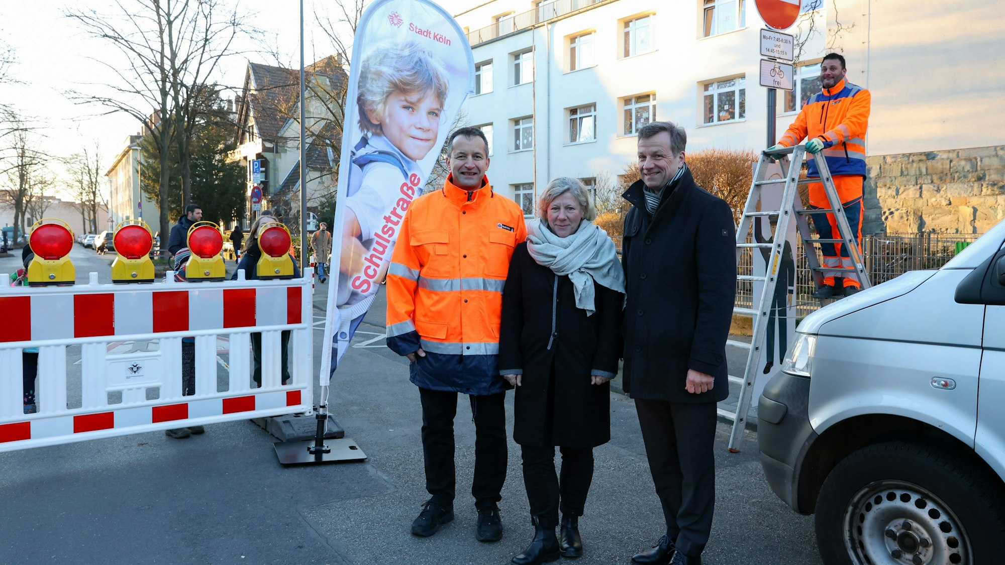 Patric Stieler, Karin Leusner und Ascan Egerer stehen neben der Bake, die die Straße absperrt. Im Hintergrund steht ein Mann auf einer Leiter neben einem Schild, das die Zufahrt verbietet.